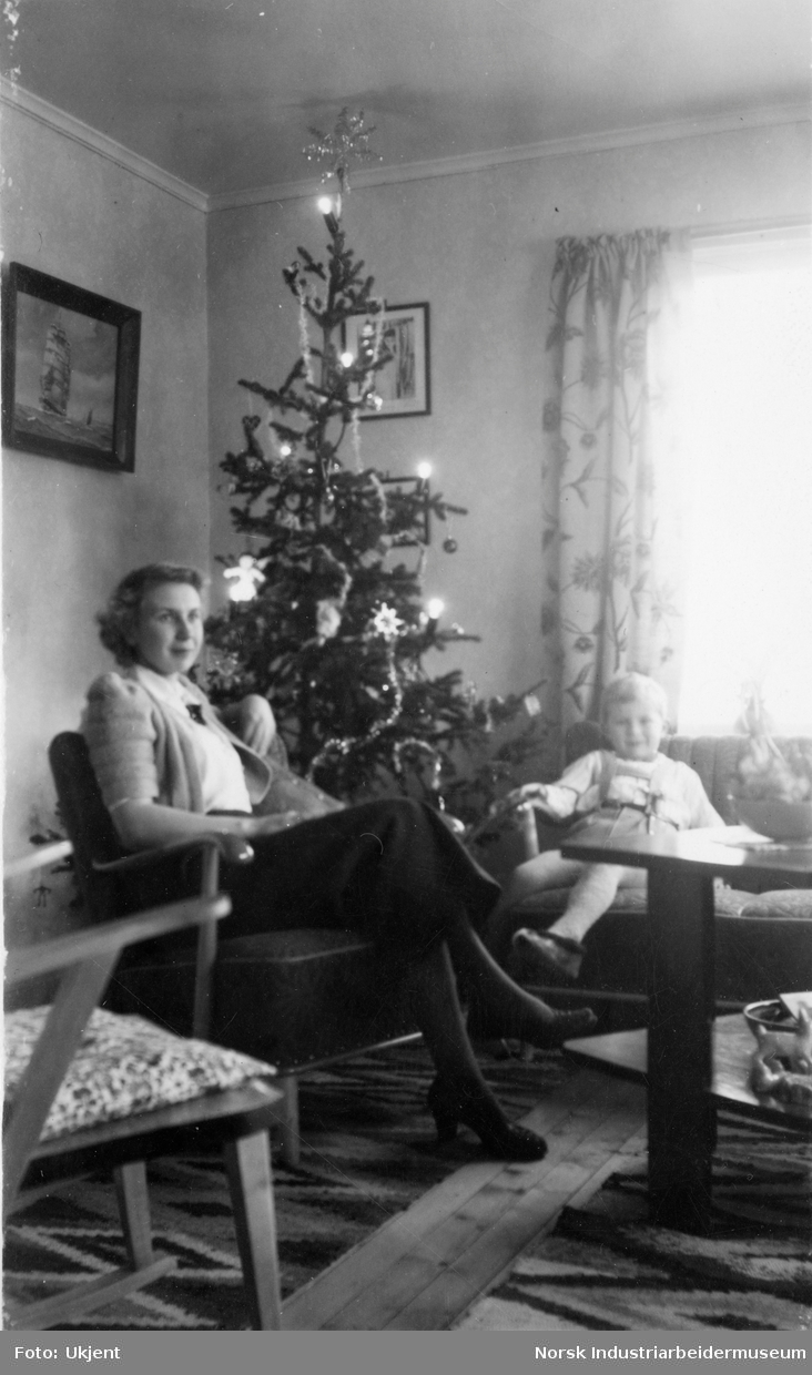 Dame med barn sittende i stue ved juletre.