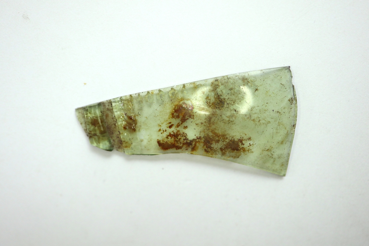 Två sammanhörande fragment av ett kägelformat passglas av gröntonad glasmassa. Pålagda strierade trådar.