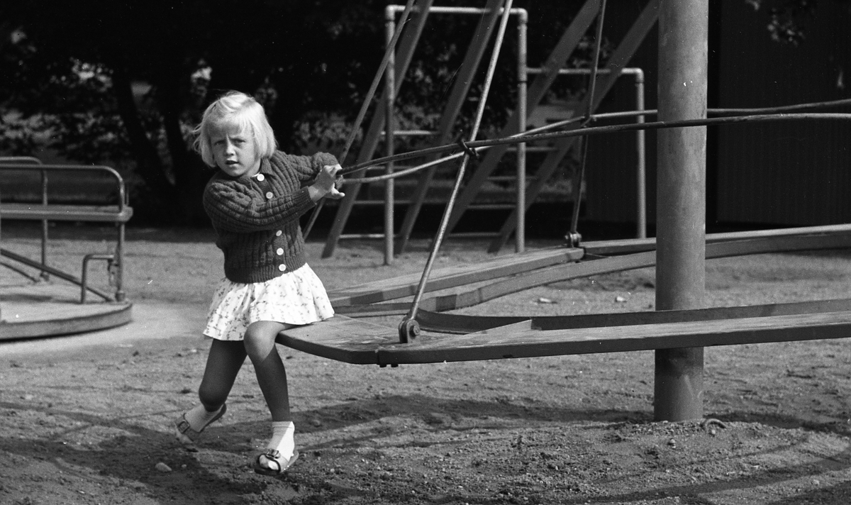 Flicka som sitter i karusell i en lekpark, Uppsala 1962
