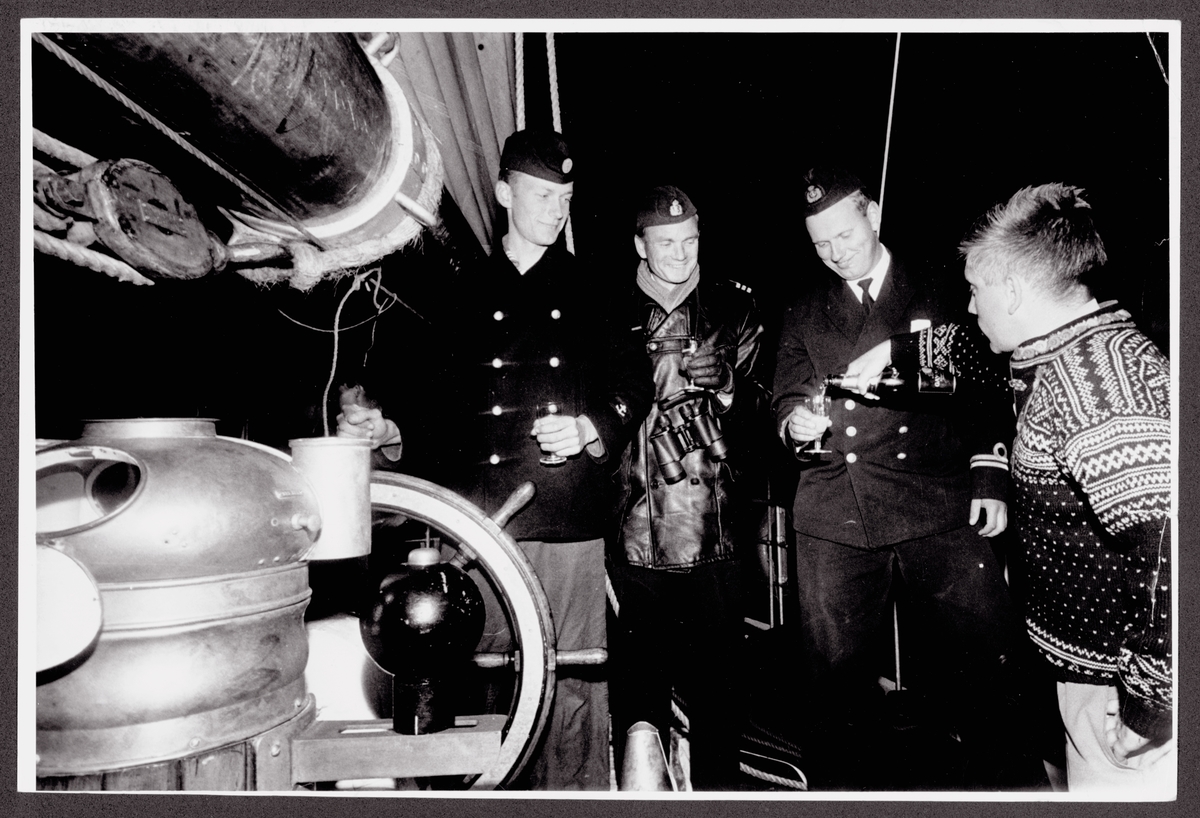Porträttbild som visar tre sjöofficerare om bord på segelfartyget Gladan eller Falken. Dem tre sjömän står vid styrratten få sina vinglas påfylld av den fjärde mannen i civila kläder. Mannen som får påfyllning är fartygschefen Lars Haller.