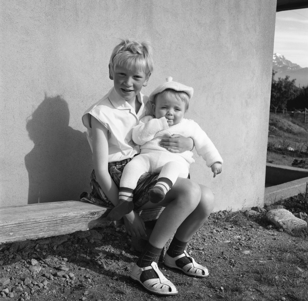 Portrettfotografi av ei jente med en baby på fanget utenfor et hus. Bjørg og Frode?