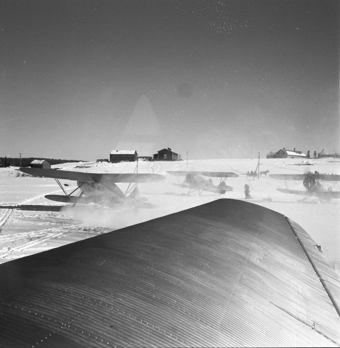 Flygfält på den tidigare sovjetiska jaktflygbasen i Märkäjärvi. I förgrunden flygplansvinge på flygplan Junkers F-13. I bakgrunden byggnader och flygplan. Efter krigsslutet vid Svenska frivilligkåren i Finland, F 19.