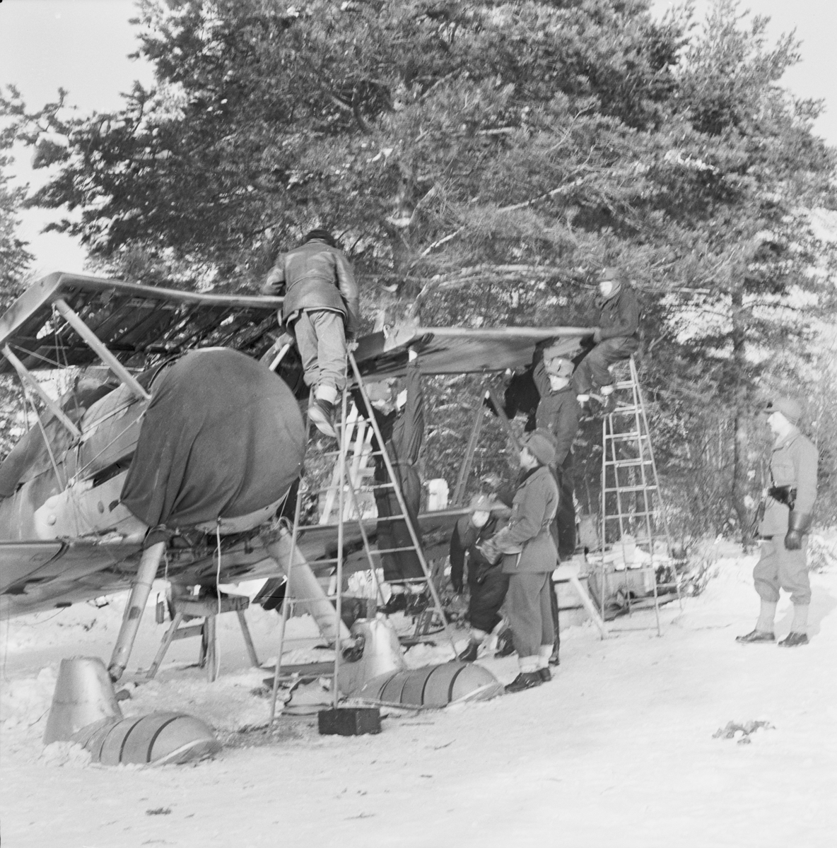 Demontering av flygplan Gloster Gladiator efter Finska vinterkrigets slut i mitten av mars 1940 vid Svenska frivilligkåren i Finland, F 19. Sju militärer i arbete vid flygplanet.