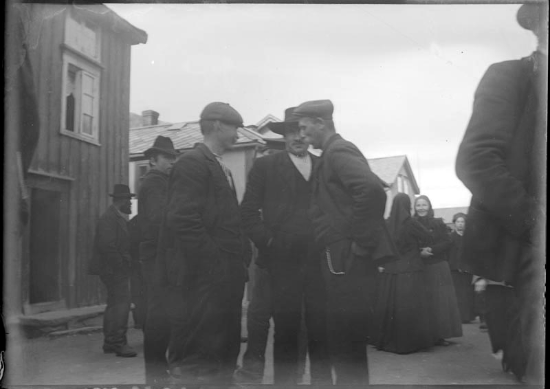 Tre menn i samtale i Sjøgata under Tiendebytte. Flere folk. Mannen til høyre er Adolf Johnsen.