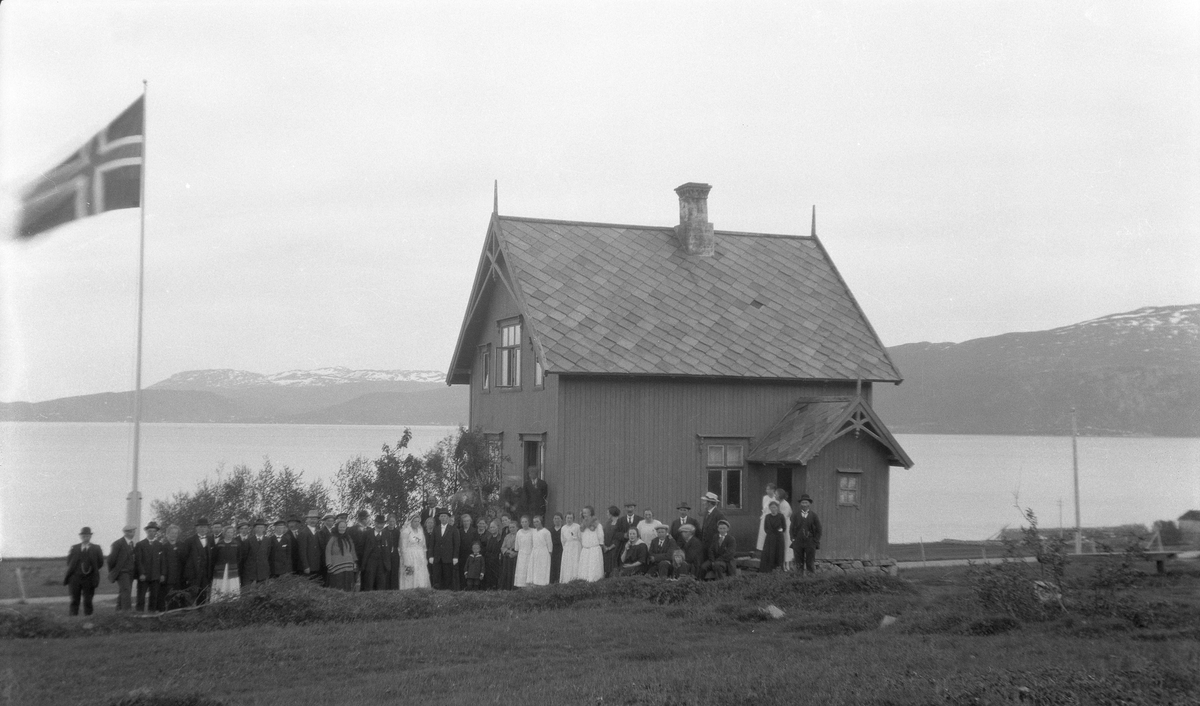 Brudepar og gjester fotografert foran hus.