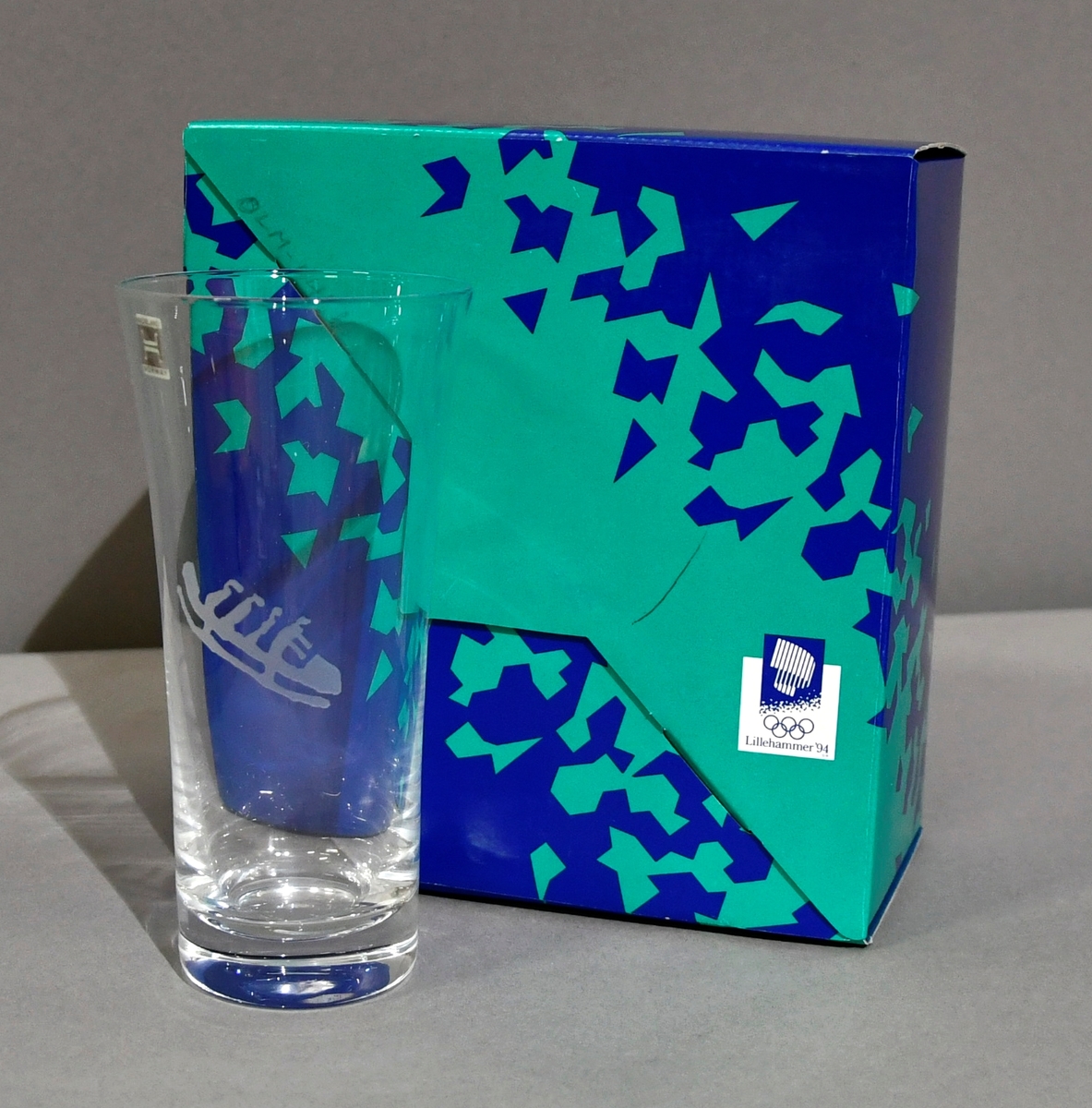 Seltersglass med frostet merke av piktogrammet for firer-bob. Glasset ligger i original emballasje.