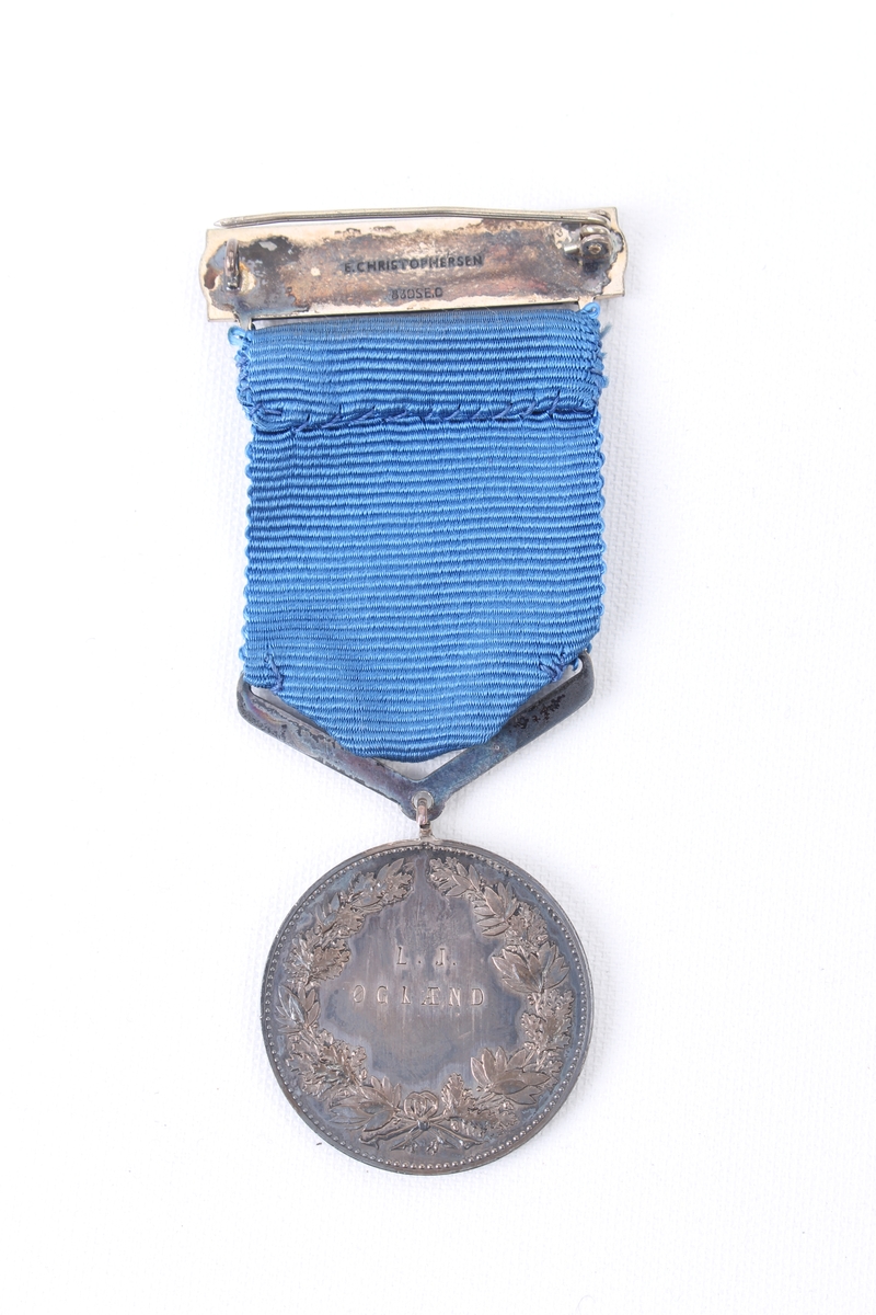 Sirkulær medalje med blått medaljebånd og agraff.