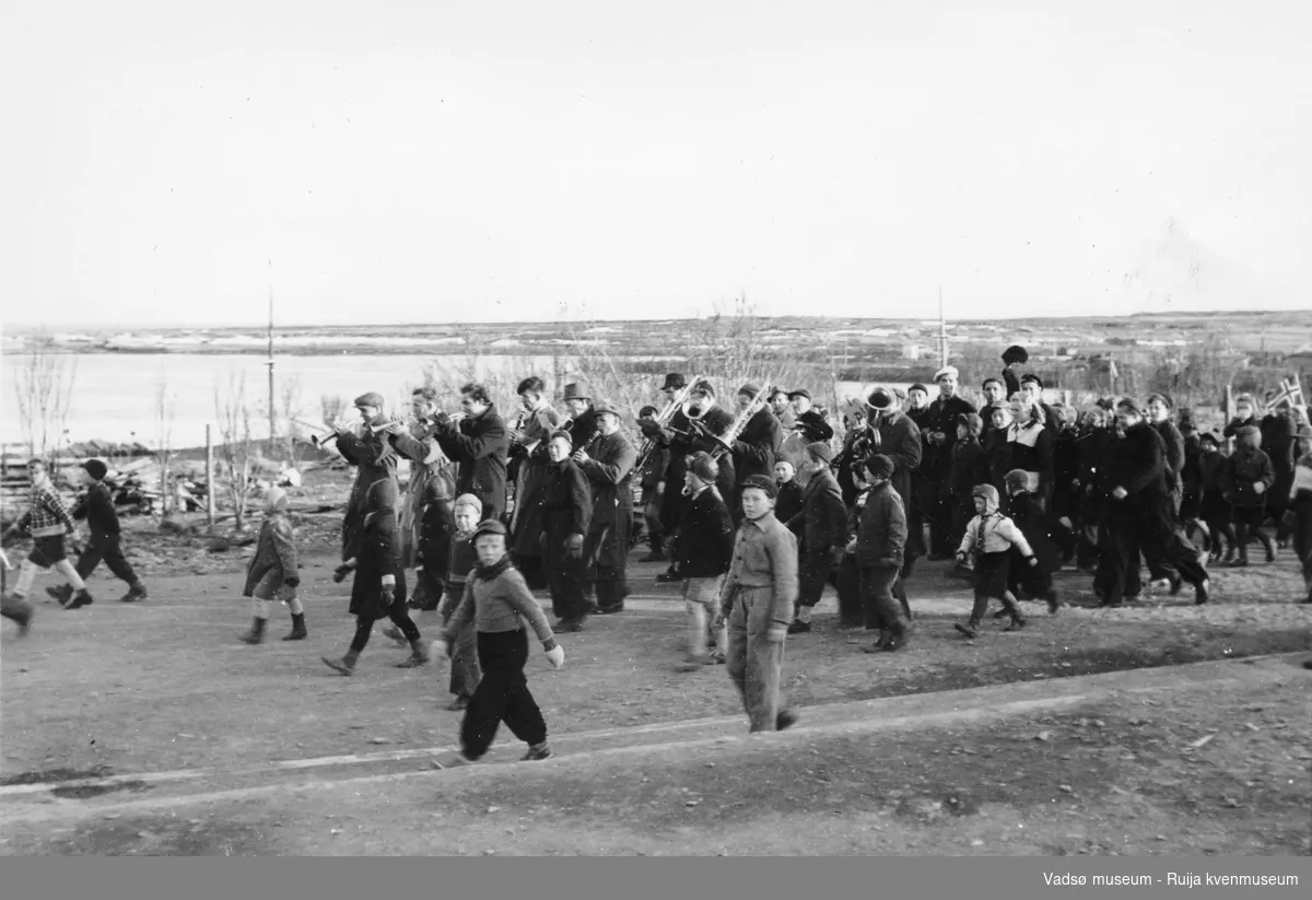 17. maitog i Vadsø 1945. Vadsø hornmusikk og barn som løper ved siden av. Bildet er tatt nedenfor skolen og kirkegården.