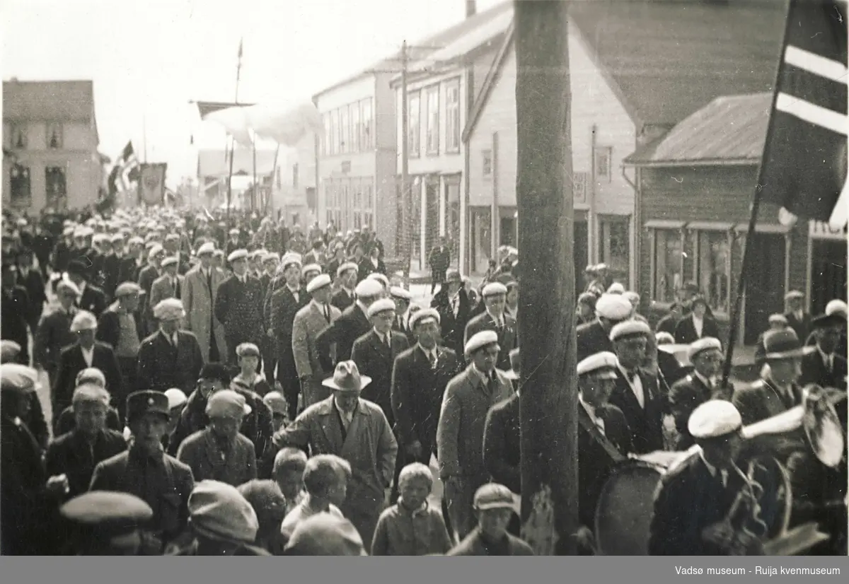Opptog i Vadsø med menn med hvite sangerluer og musikkorps. Feirer byens 100 års jubileum i 1933.