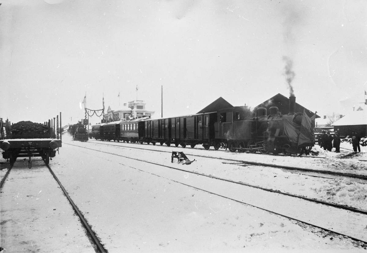 Invigning av  Eksjö - Österbymo Järnväg vid Eksjö station 17 december 1915. Loket till höger,  EÖJ lok 1 är utsmyckat med en fanborg. Bakom loket syns EÖJ:s persontrafiksvagnar, två resgodsvagnar och tre personvagnar.
Längst till vänster syns stolpvagnar, delvis lastade med kol.
