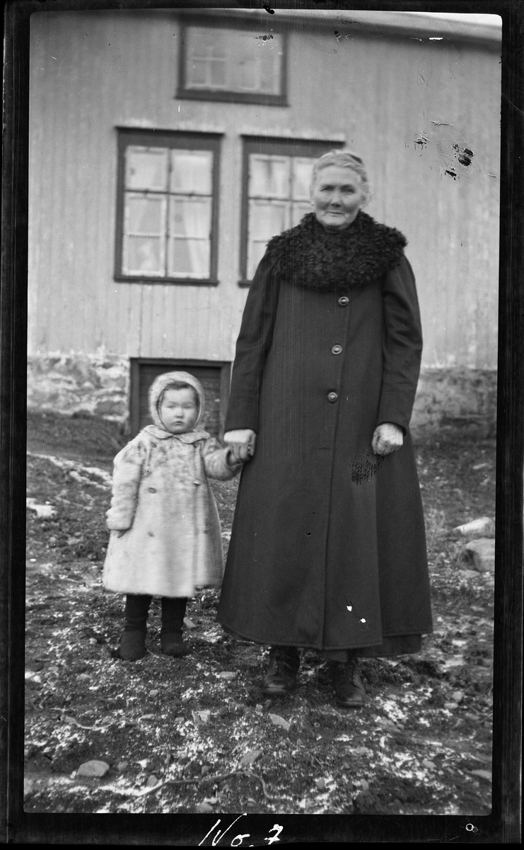 Portrett av bestemor med barnebarn stående på gårdsplass.