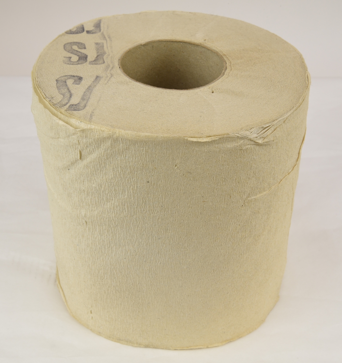 Toalettpappersrulle av svagt kräppat papper. Rullen är stämplad SJ på ena sidan med en mörk färg.