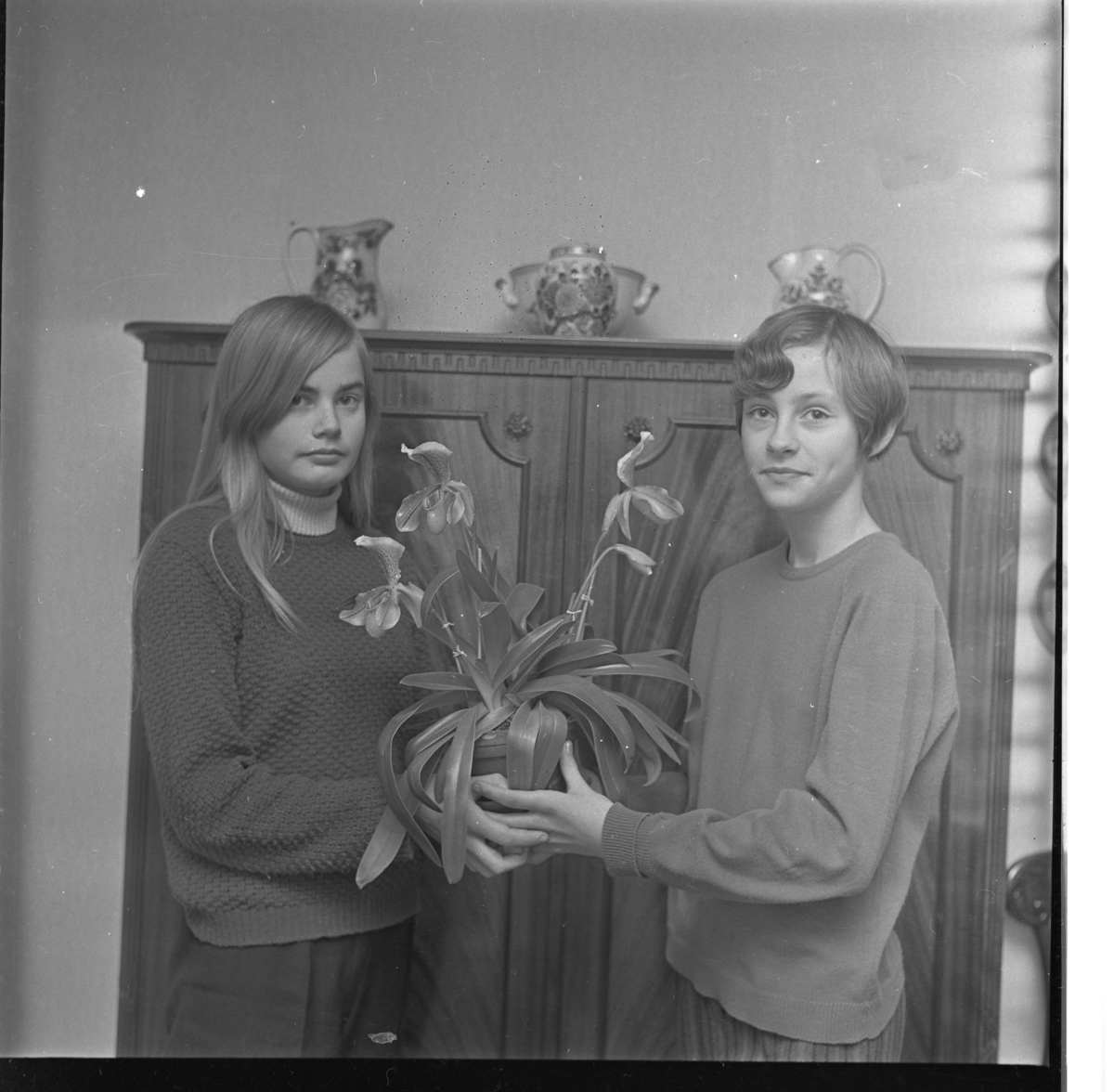 Två flickor står framför ett linneskåp och håller en orkidé mellan sig. Elisabeth Pyhäsalmi står till vänster och Elisabeth Josefsson till höger.