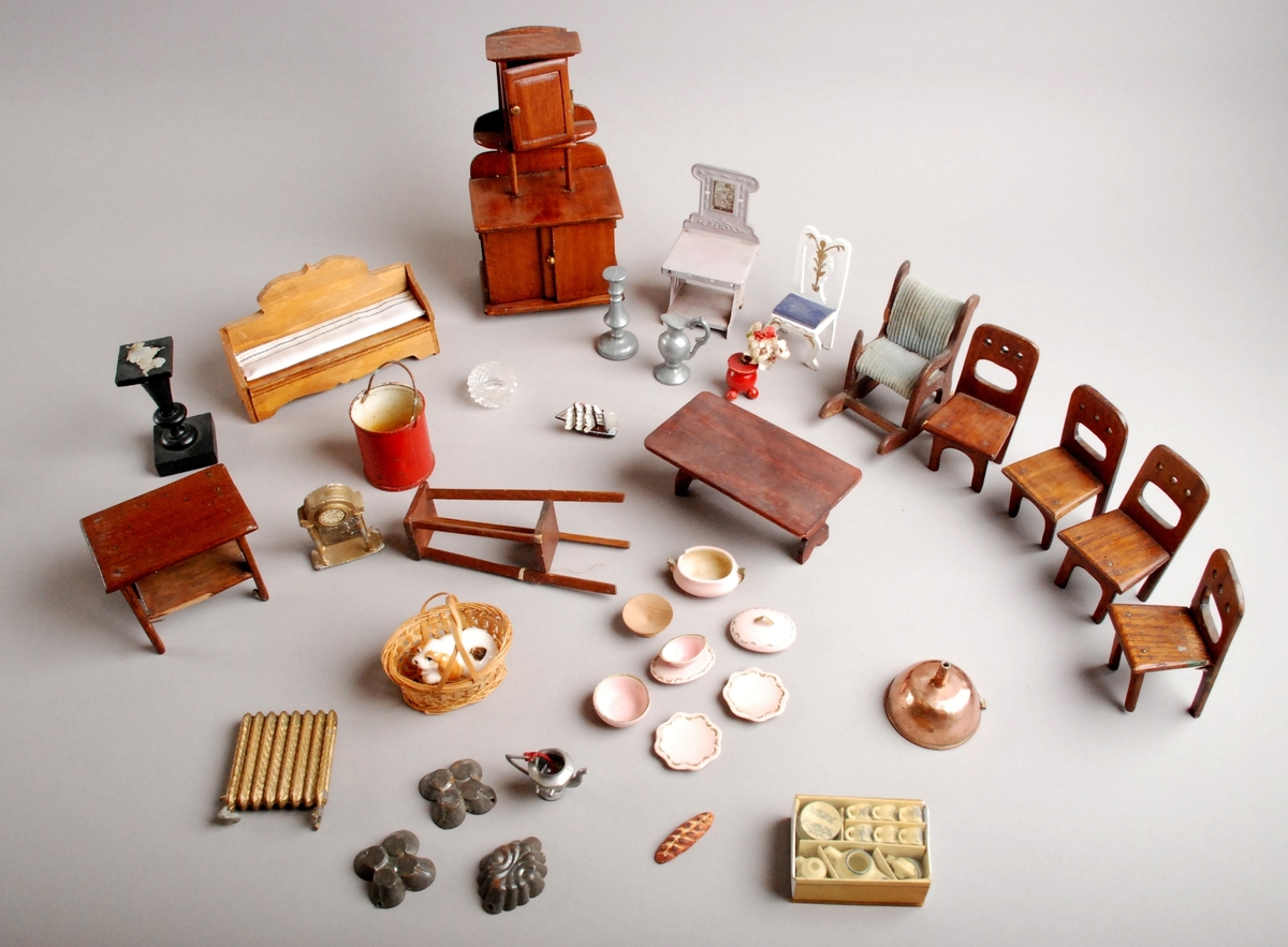 Kasse med løst inventar til dukkehuset (GB20202a). Inventaret består av møbler, tekstiler, kjøkkenutstyr, servise og bestikk m.m. Gjenstandene er avbildet på utsiden av kassen.