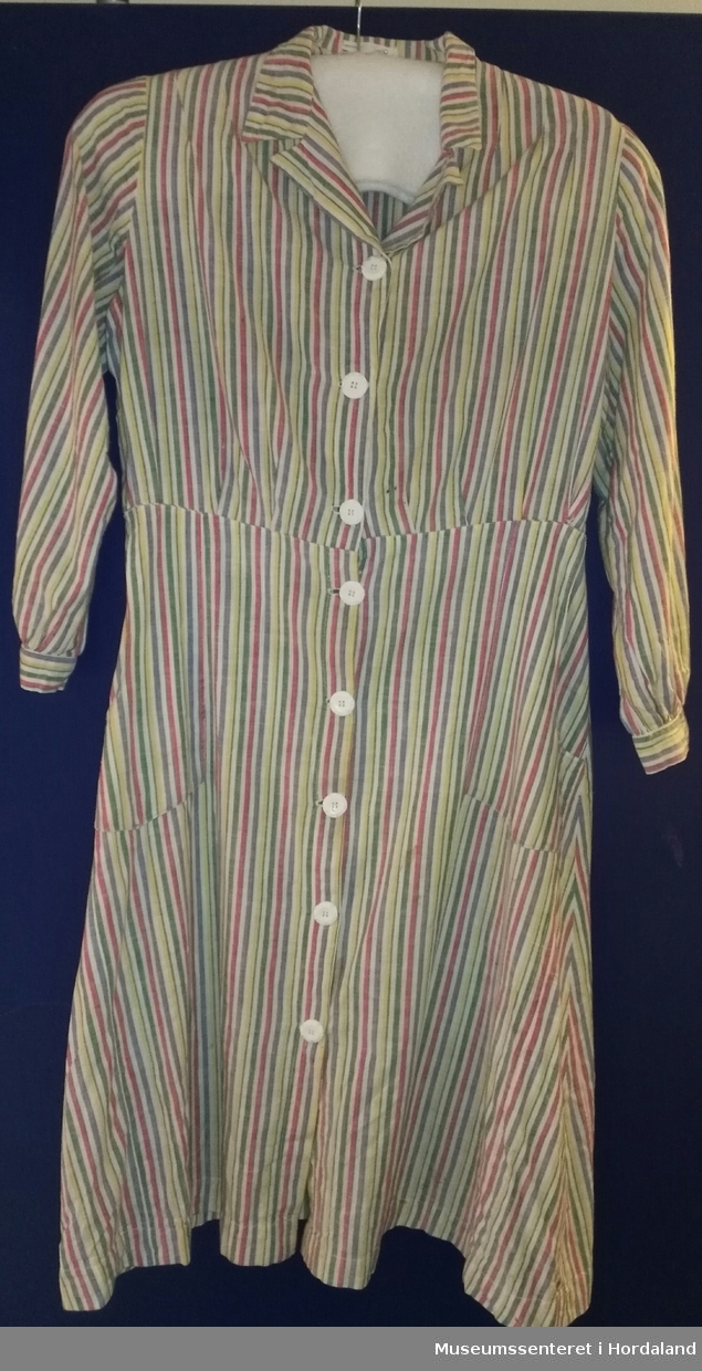 Heimesydd kjoleforkle i bomull med lange ermer og krage. 8 kvite knapper og lommer i front. Raud-, kvit-, blå- og grønstripa stoff.