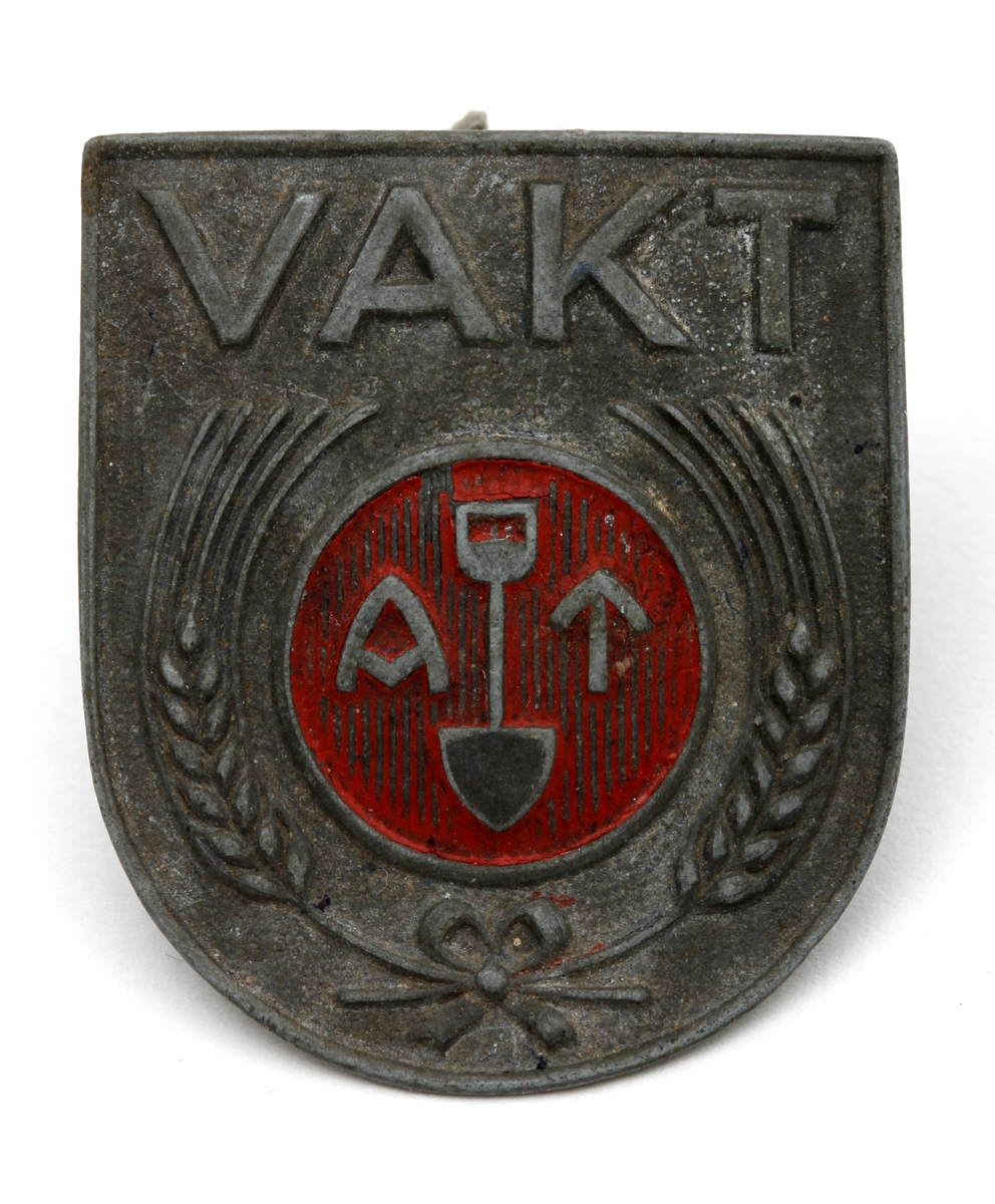 Jakkemerke fra andre verdenskrig, brukt i den tyske arbeidstjenesten
med symbol som består av en spade mellom bokstavene A og T,  omkranset av to sambenbundede kornaks
