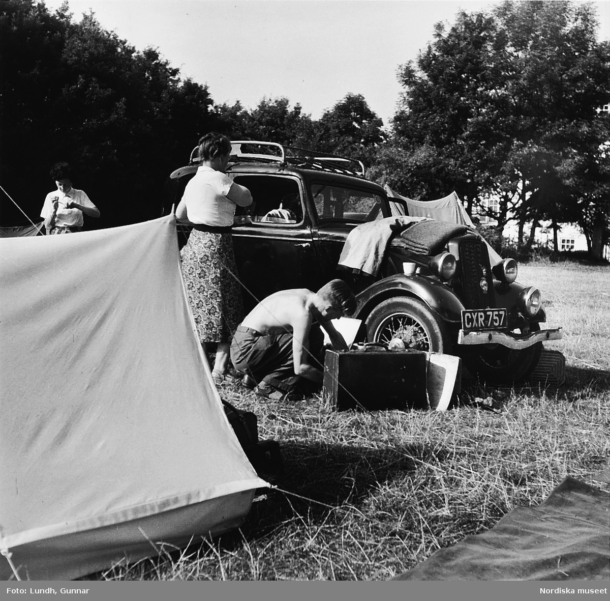 Två personer med packning vid en engelskregistrerad Ford Y årsmodell 1934. I förgrunden ett tält.