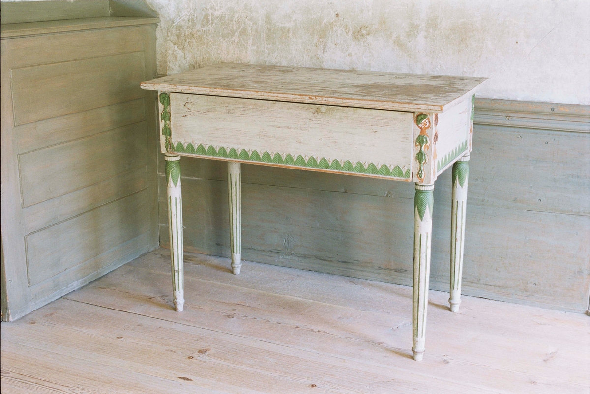 Mössbord i gustaviansk stil med låda, av furu målad i en gråvit färg.
Rektangulär rak form, höga sarger med bladformad pastellagedekor i grönt.
Svarvade bladhölstrade ben med kannelyrer, ifyllda med grönt.
