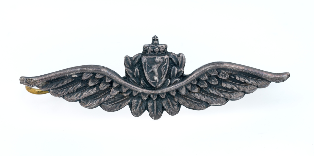 Luemerke i sølv. Utformet som flyvervinge med sentrert riksvåpen.