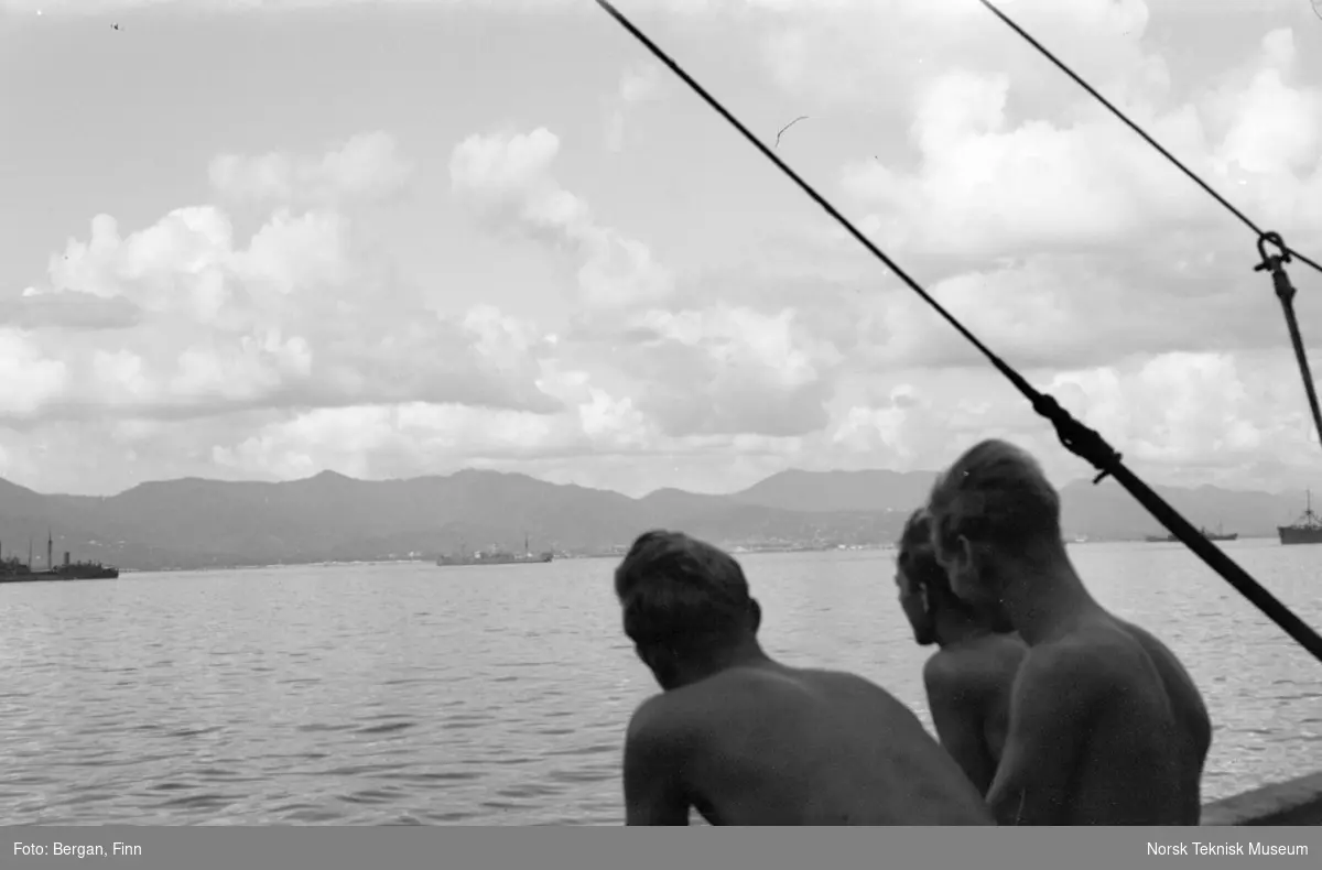 Tre personer ombord på skip, ser inn mot havneområde, Port of Spain