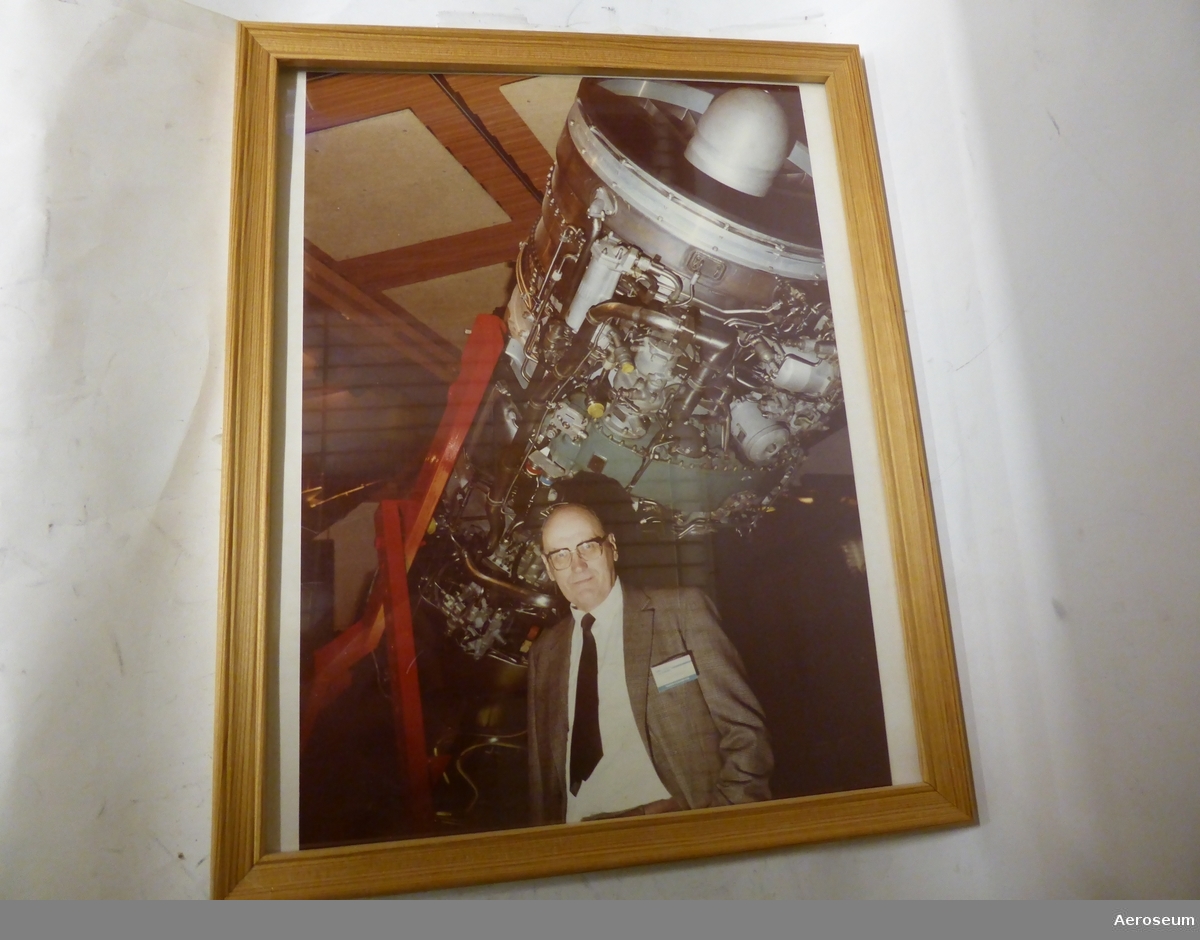 En grå och svart pärm med ett färgfoto i träram. Fotot föreställer Evald Wedin framför en jetmotor, troligen RM6. Med fotot föjer ett kopierat tidningsurklipp och ett årsmötesprotokoll från Flygtekniska Föreningen från 1985 där det meddelas att Evald Wedin tilldelats Thulinmedaljen.