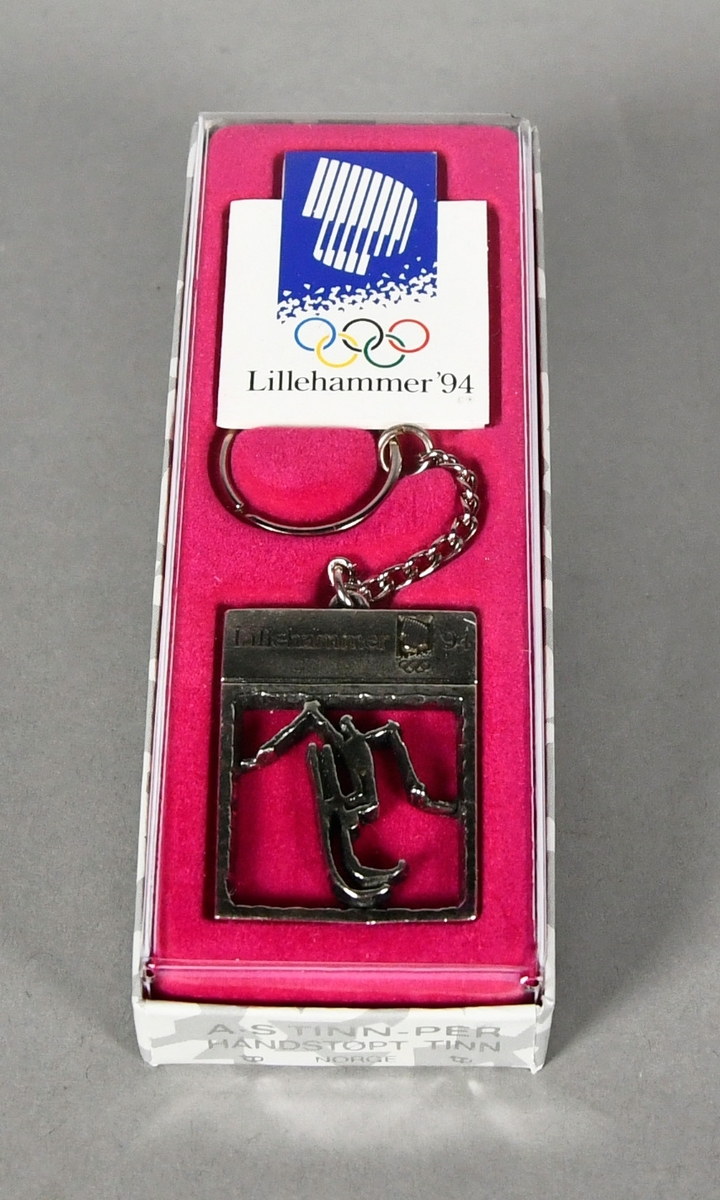 Nøkkelring med rektangulært anheng med piktogram for freestyle. Nøkkelringen ligger i original emballasje på rosa underlag.