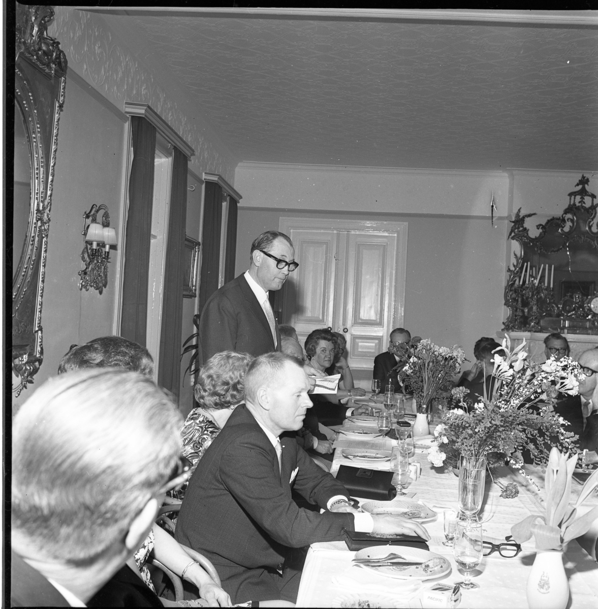 Festklädda män och kvinnor sitter vid matbord i samband med Gränna Sångsällskaps 30-årsjubileum. De är möjligen på Ribbagården eller Hotel Brahe. Mannen som står upp är Nils Jarenskog och hitom honom sitter Karl-Erik Karlsson.