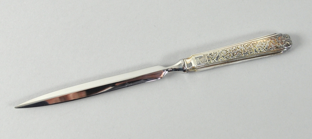 Brevkniv av sølv med krystallmønster og logo for Lillehammer '94 inngravd på skaftet. På baksiden er det inngravert piktogrammer.