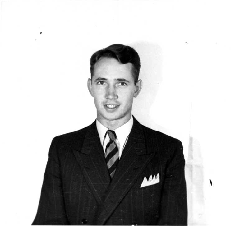 En ung man i kritstrecksrandig kavaj med näsduk och tvärranding slips.