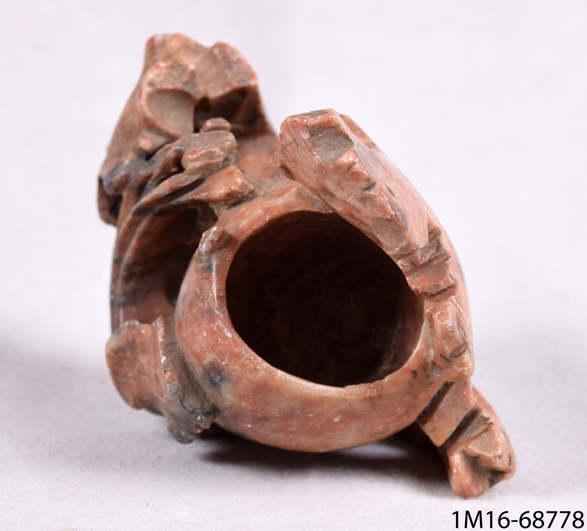 Cigarrkopp av brunspräcklig marmor, 3/4-äggformad och omgiven av blomornamentik.