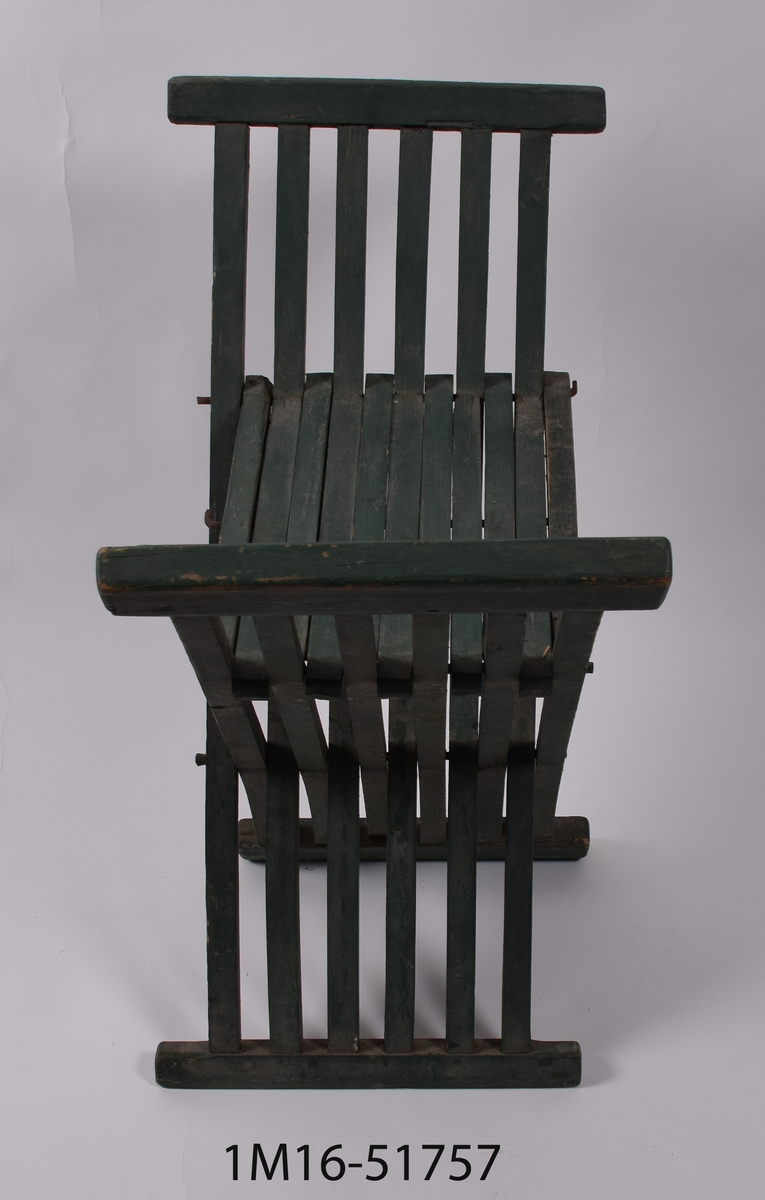 Grönmålad trädgårdstol utan ryggstöd, bestående av fyrsidiga träribbor och ihopfällbar från sidorna.



Neg.nr: 981/1051:2