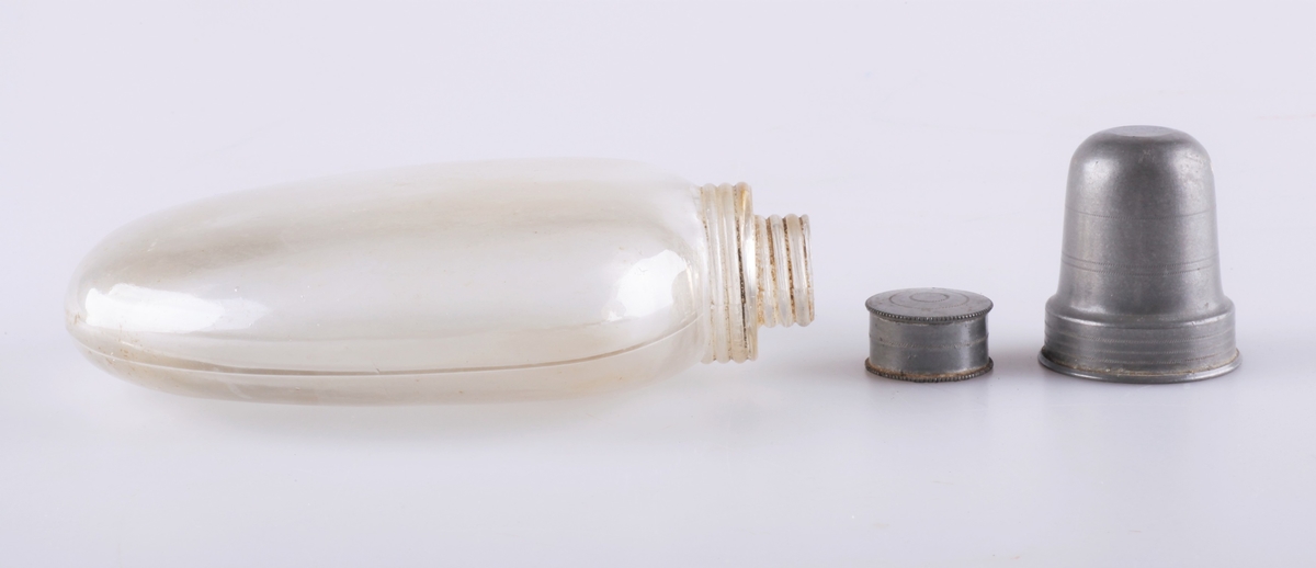 Lommelerke (a) av klart glass, skrukork av metall (b) med kork innvendig. Tilhørende drikkebeger (c) av metall som skrus på flaska. Skrukorken er dekorert med inngraverte sirkler.