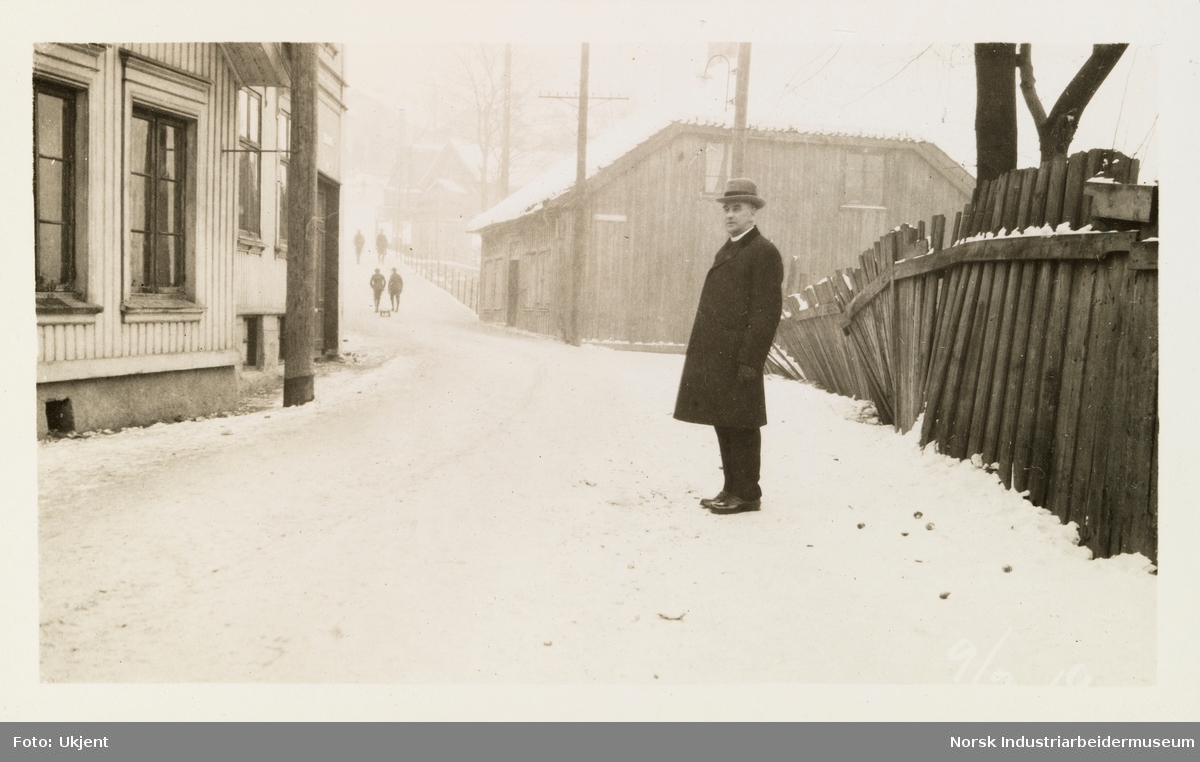 Mann står i gate med trehusbebyggelse på vinterstid