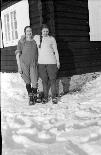 Øksendalen. Gruppe nr. 2 fra Gudbrandsdal Fylkesskole. To kvinner i skiantrekk utenfor tømmerhytte med torvtak. Vinter.