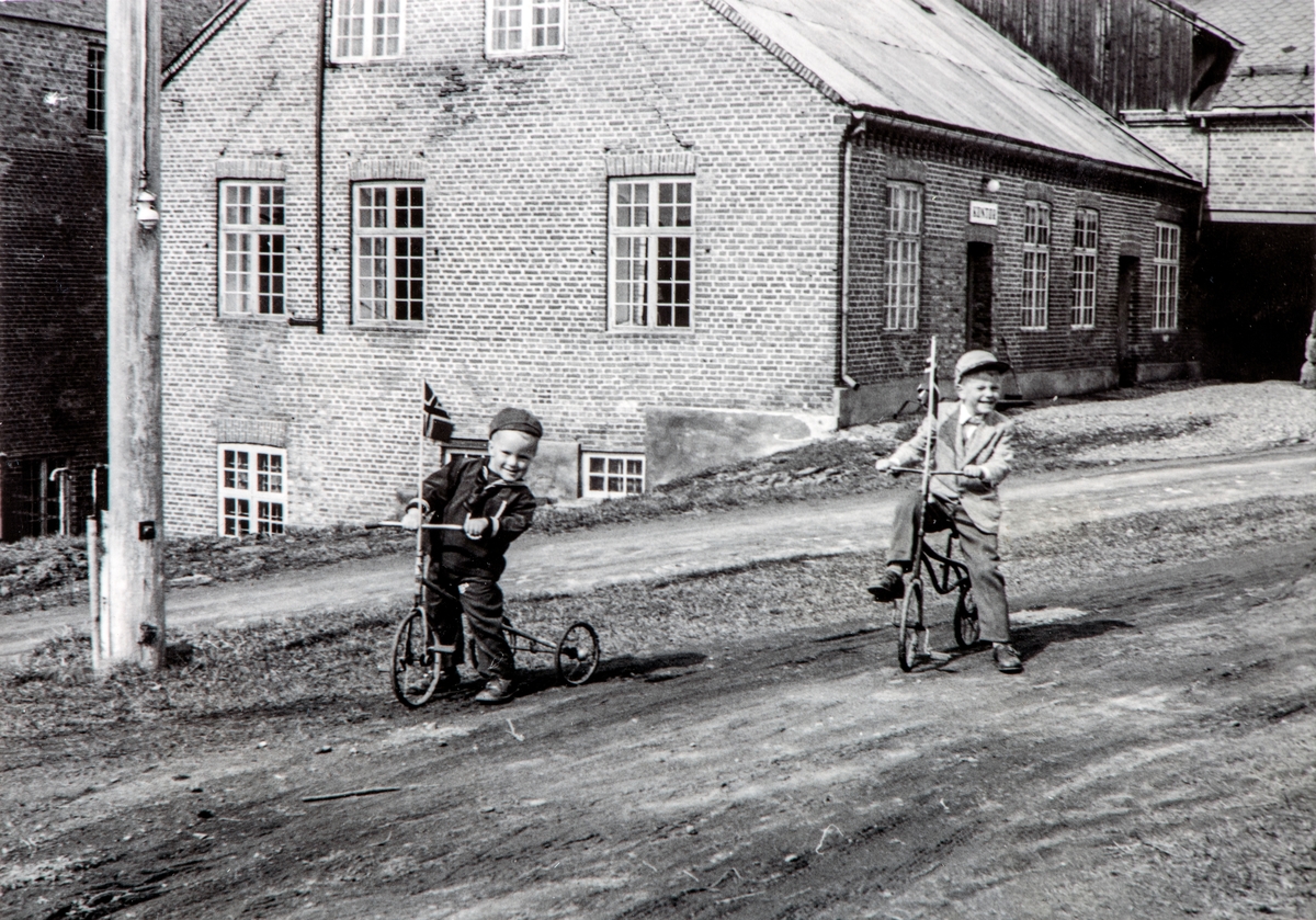 Atlungstad brenneri, Stange. Erik Gjestvang og Jon Gjestvang, foran kontorbygningen. Trehjulsykkel, 17.mai, flagg.