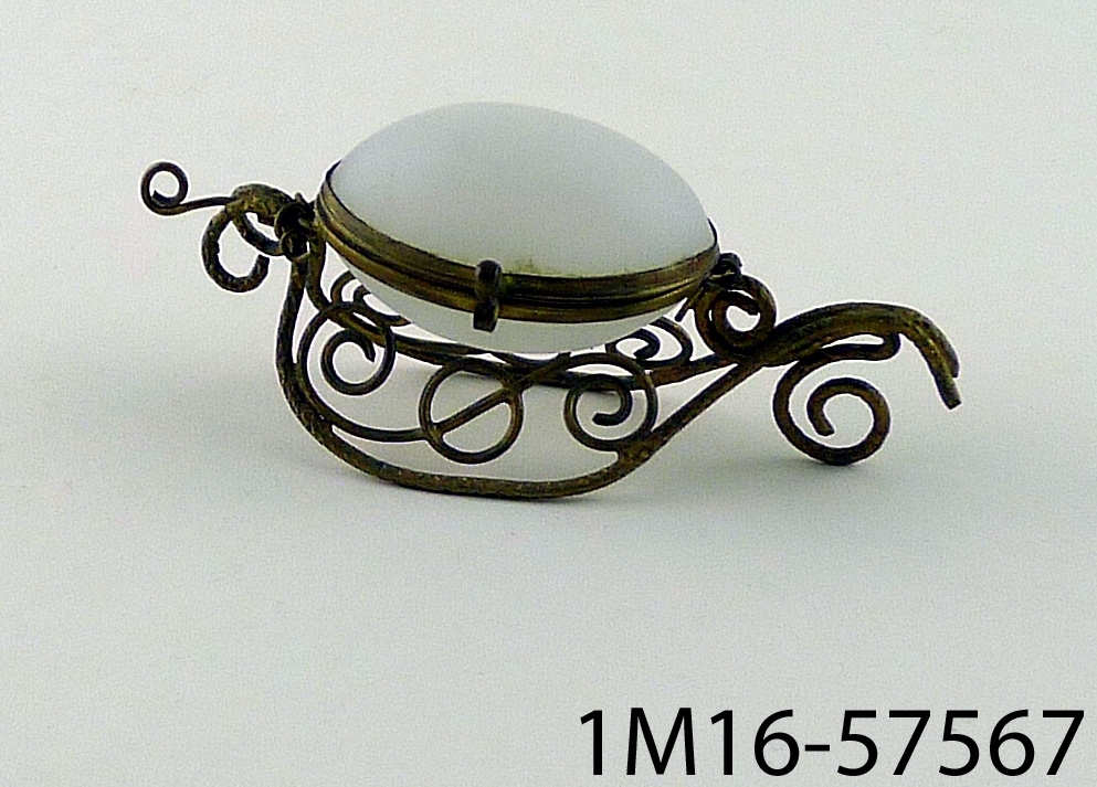 Nipperask, äggformad,  av vitt opakt glas med fotställning av i ornament böjd mässingstråd.