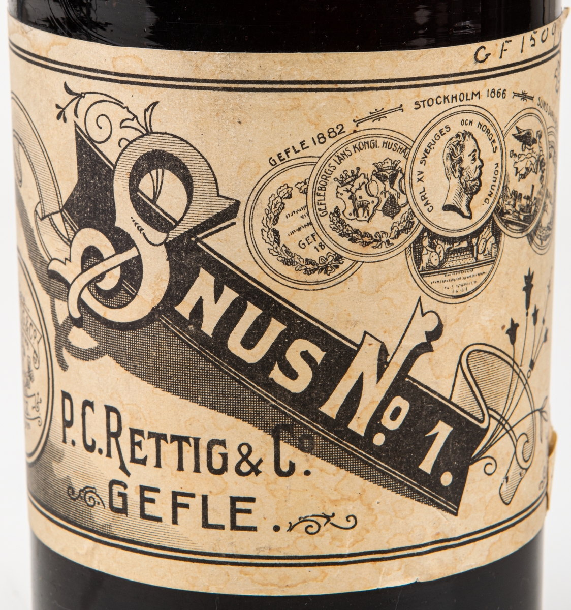 Snusflaska, mörkbrun flaska med ganska vid hals med kork. Etikett: "Snus nr 1, P.C. Rettig & Co, Gefle". Guldmedalj 1882 Gefle, 1866, Stockholm, 1882 Sundsvall.