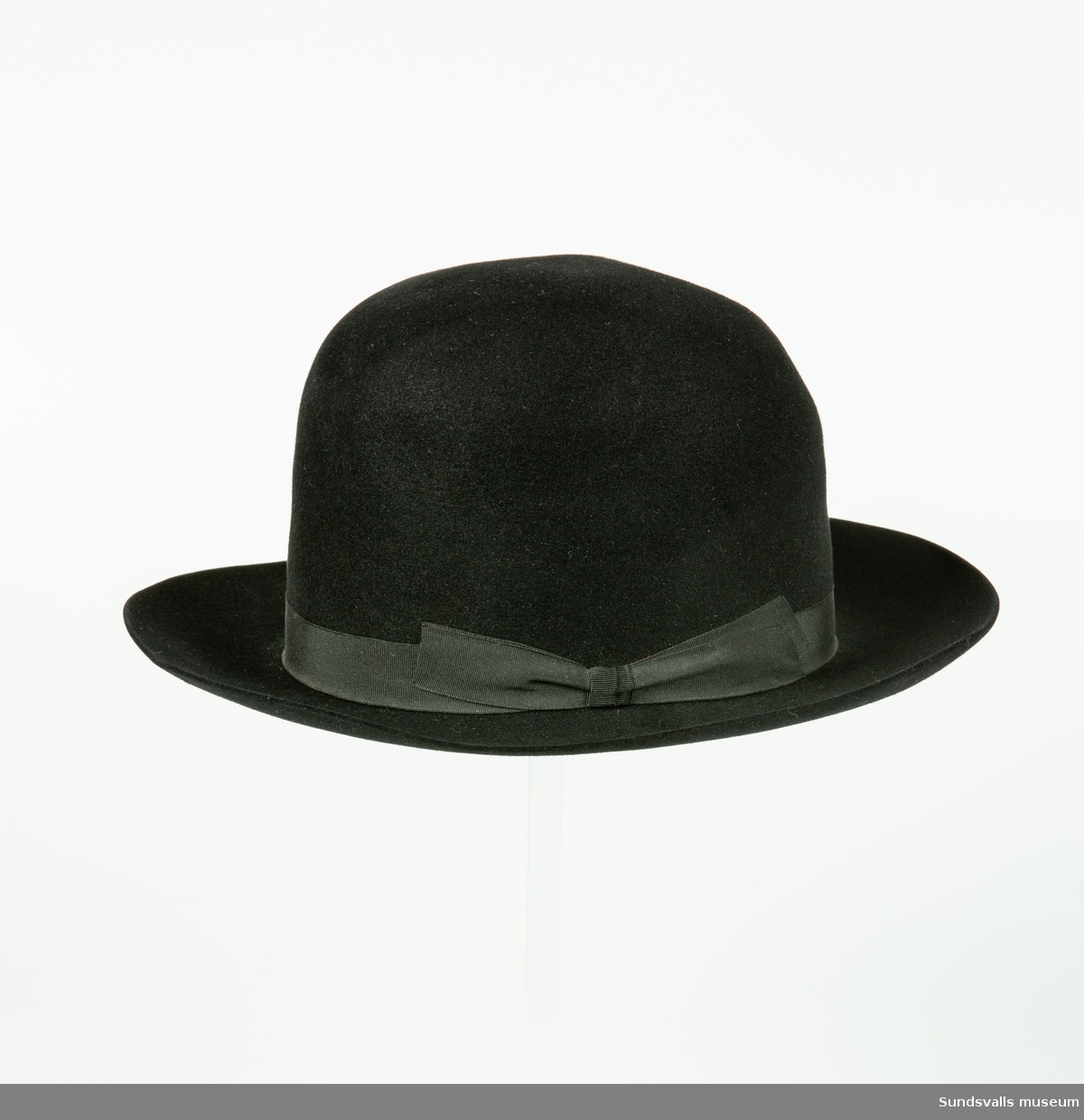 Svart herrhatt med stukad kulle och svart band. I läderbandet på insidan av hatten är 'JD' utstansat. Hatten är också märkt 'Dobesch Wien Deluxe Import'.
