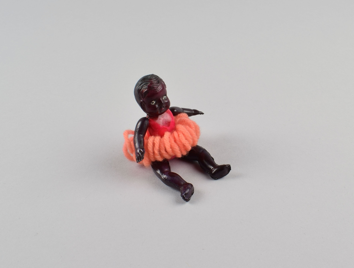 Liten figur av sort jente med ballettdrakt. Tutu laget av garn. Bevegelige armer og ben festet med innvendig tråd.