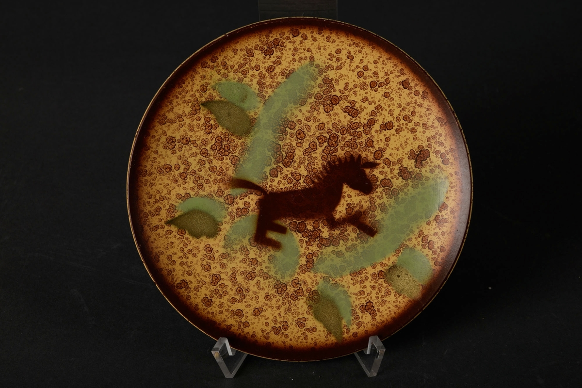 Lysebrunt asjett med mørkebrun dekor av en hest, og grønne blader.