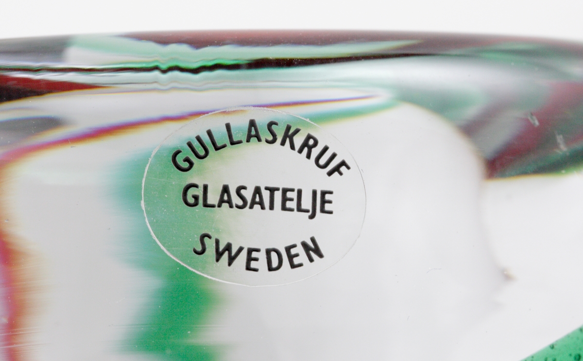 Mindre skål färgad med två vridna grön-vinröda linjer.
Etikett. Ofärgad med svart text "Gullaskruf // glasateljé // Sweden"