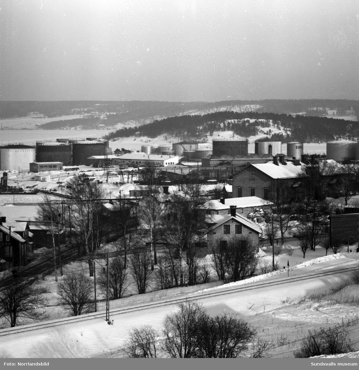 Vy från Skönsmon mot Vindskärsudde och Alnö. I nederkant järnvägen och gammal bebyggelse på Skönsmon, längre bort oljehamnen, Tjuvholmen och Alnö.