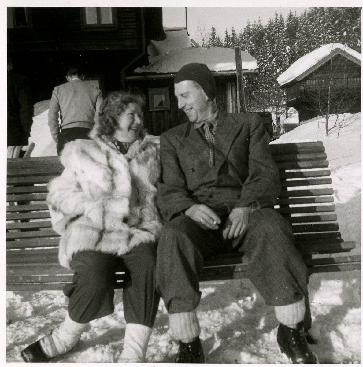 Én mann og én kvinne sitter på en benk i vinterlandskap. Usikker på hvem de er.