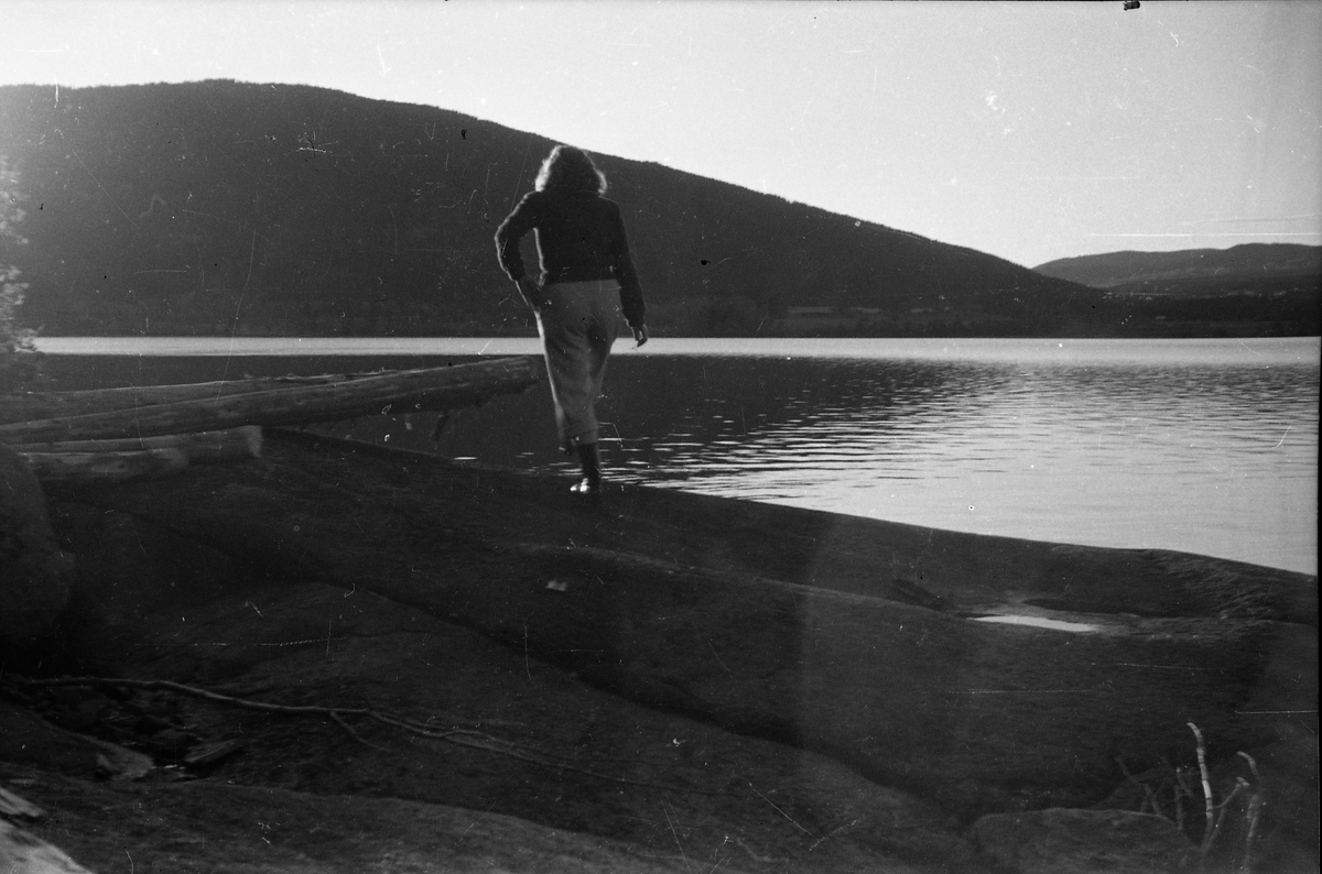 Avfotografert bilde med utsikt over en innsjø. En uidentifisert person inne på stranda. Stedet er ikke identifisert.