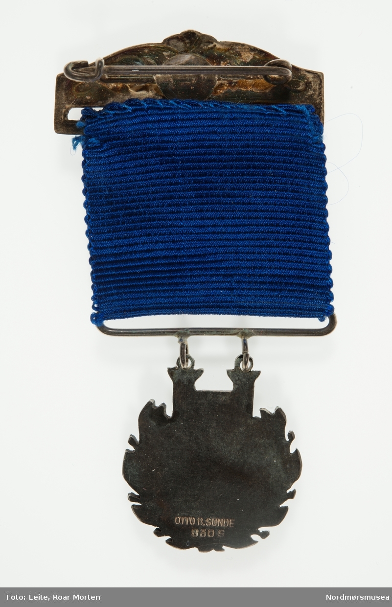 Rund medalje med stilisert lyre og krans. Blått bånd