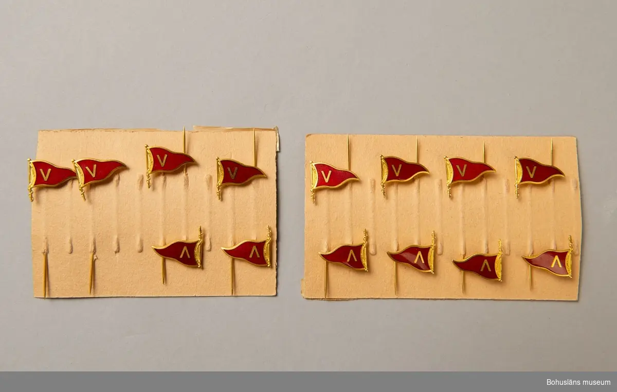 Två kartor med klubbnål för Segelsällskapet Viken, Uddevalla, den ena med sex och den andra med åtta nålar. Märket i form av vimpel i rött med guldfärgat V, vilket är sällskapets symbol. Förvaras i UM023566:1.