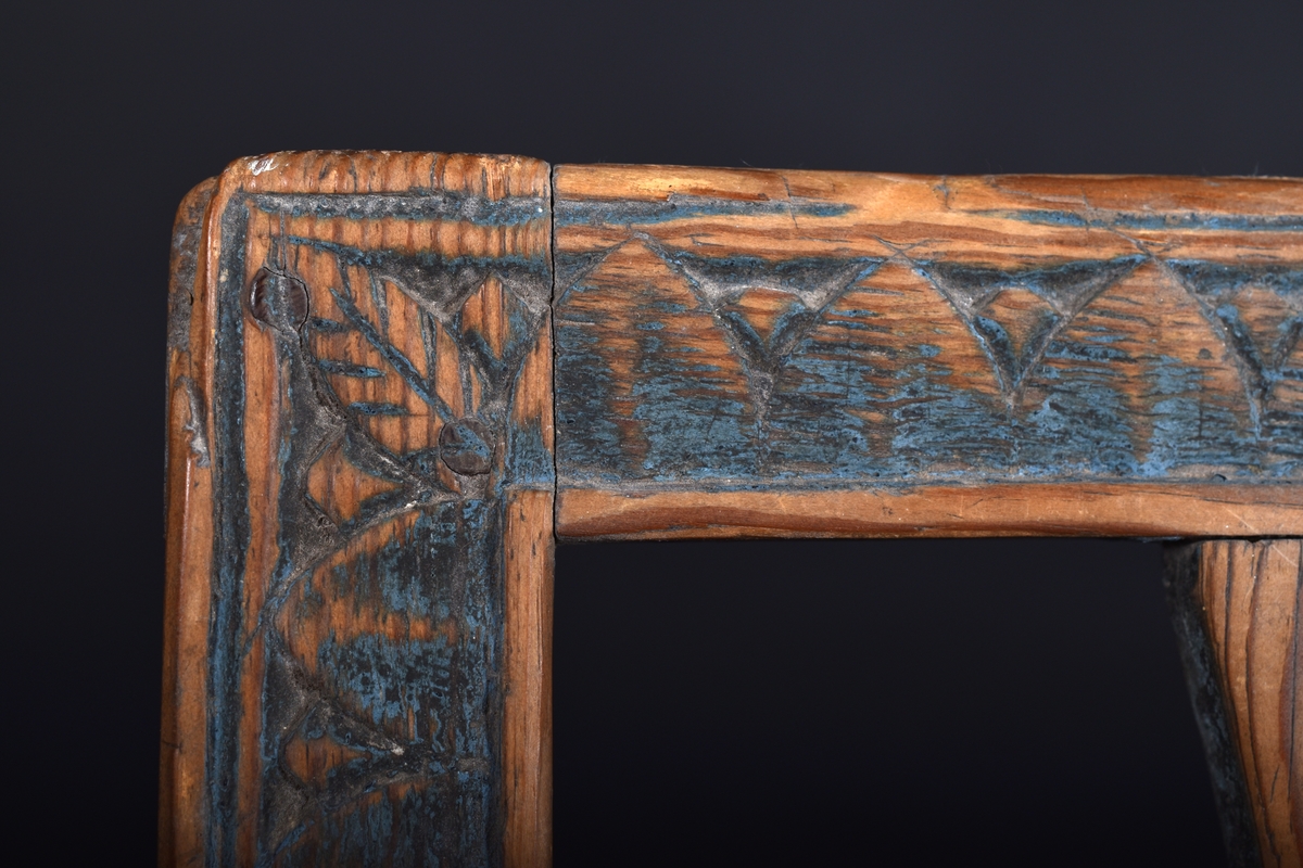 Stol i furu, en av två, med fyra raka ben som nedtill är förbundna med slåar, den ena mycket nött. Rygg med rektangulär ram prydd med bladstav samt en genombruten mittplatta. Ursprungligen blåmålad, färgen kraftigt bortnött.