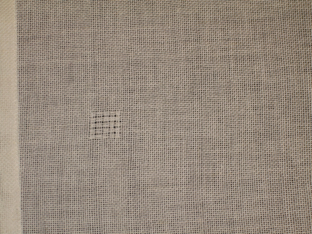 Vävprov på gardin i bomull i vitt med med 1,2 mm turkos kanter. Provet är vävt i tuskaft med fyra rutor vävda i myggtjäll. Komponerad av Ann-Mari Nilsson. det är fyra hål på ena kanten efter att den suttit ihop med en kollektion av gardiner.