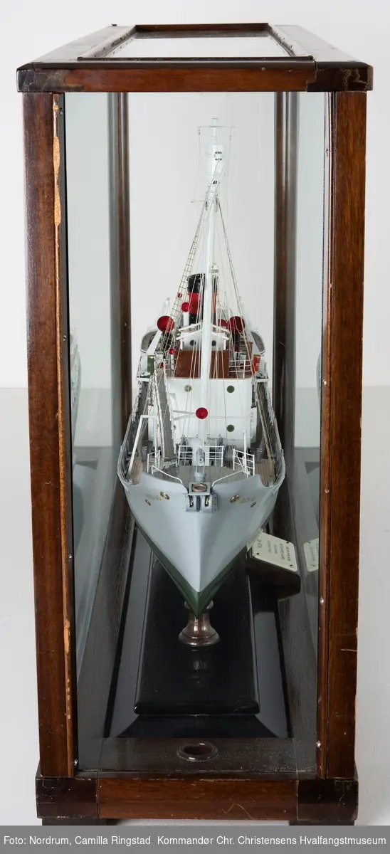 Miniatyrmodell av hvalbåten "Kos 40" tilhørende Hvalfangstselskapet Kosmos A/S i glassmonter. Skipet ble bygget ved Smiths Dock Co. Ltd. Middelsbrough, U. K. Modellen har tidligere tilhørt skipsreder Anders Jahre.