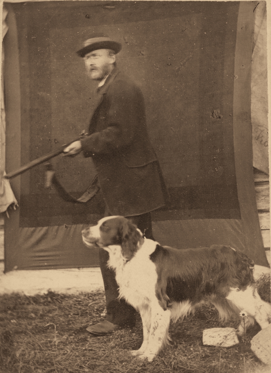 Portrett av Andreas Sellæg med hagle og hund, tatt utendørs foran et provisorisk bakteppe.